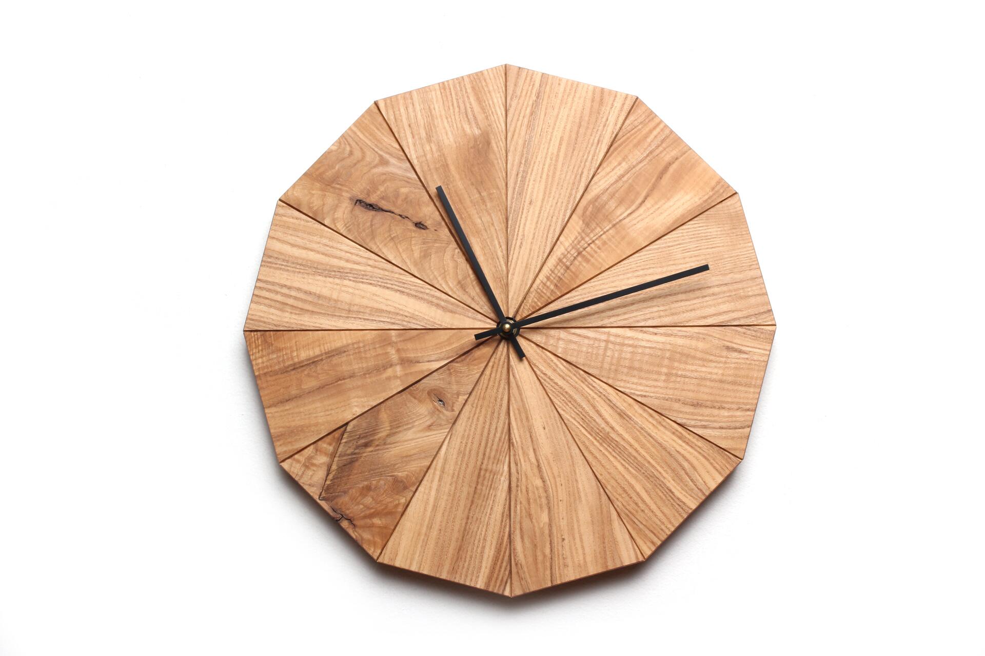 Wooden clock with a geometric, fan-like design, featuring black hands on a white background.