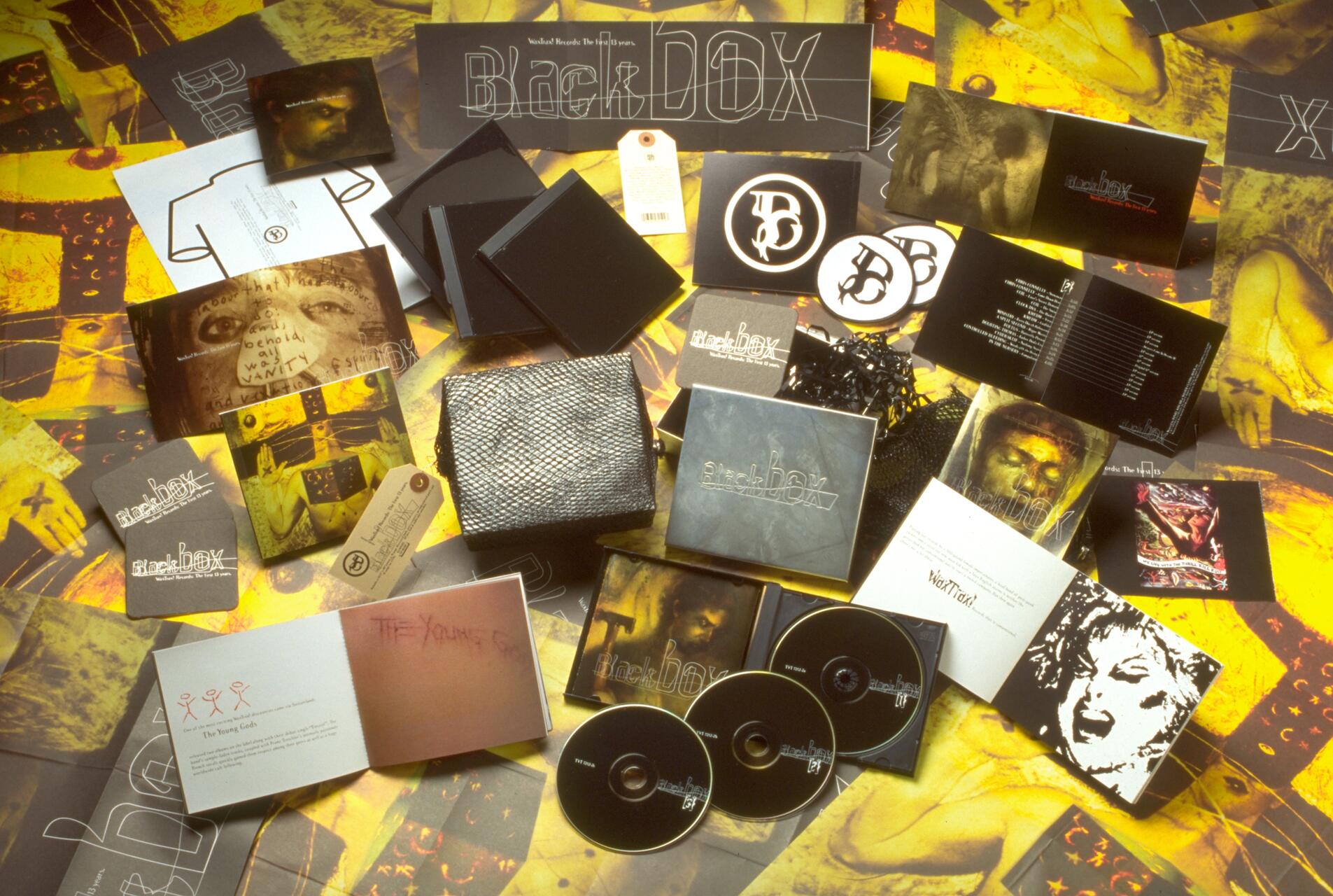 Assorted music album materials with CDs, booklets, and graphics on a yellow and black patterned surface.